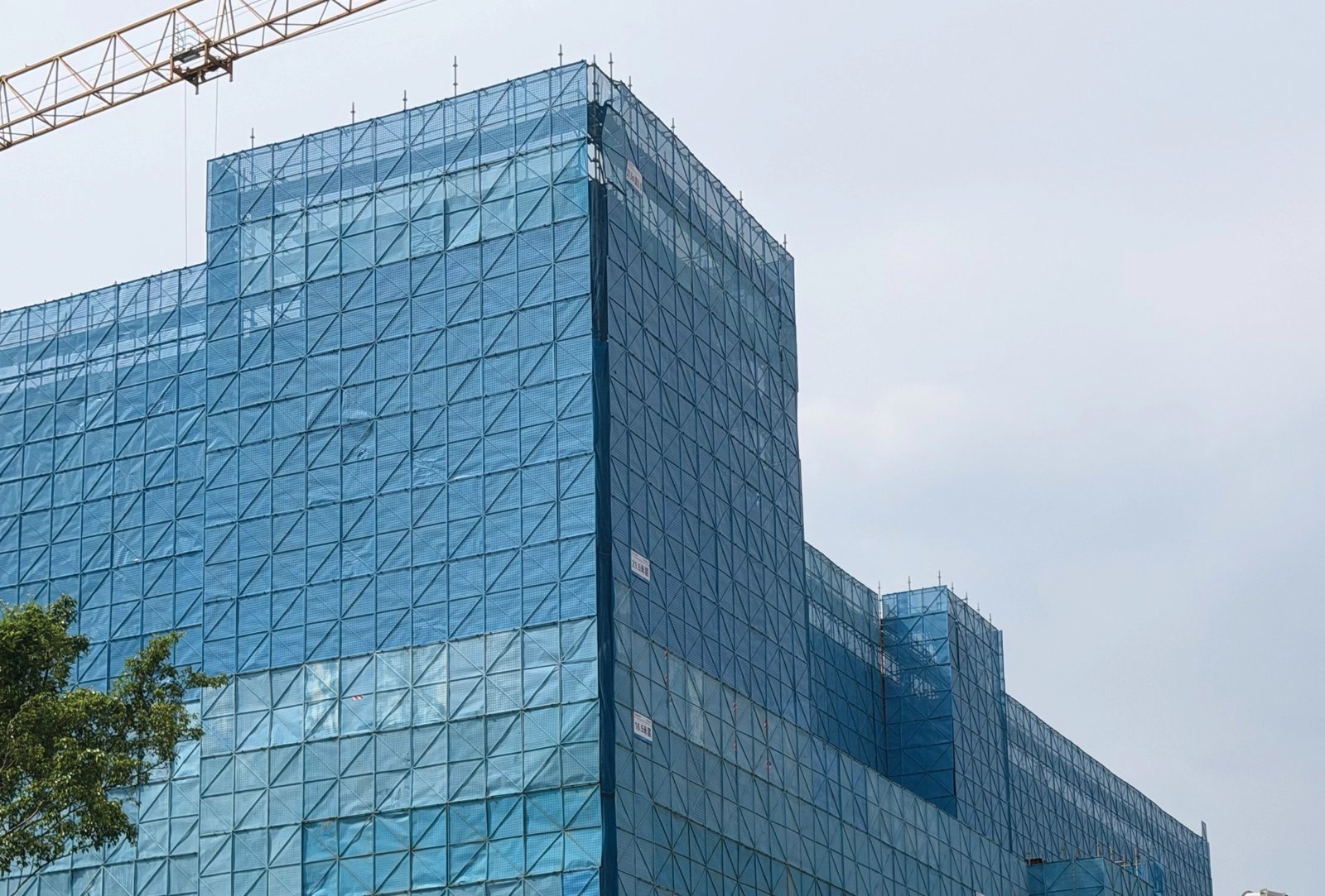 Zhaoqing Southern Power Grid during facade installation: scaffold, safety mesh, and crane over the stepped volumes