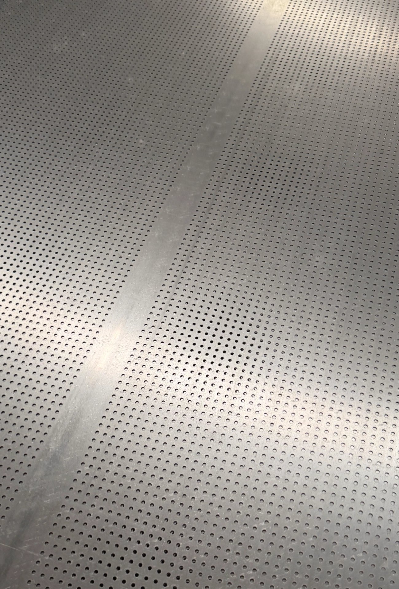 Close-up of a LINDELACR punched aluminum sheet: staggered circular holes and a solid vertical ligament