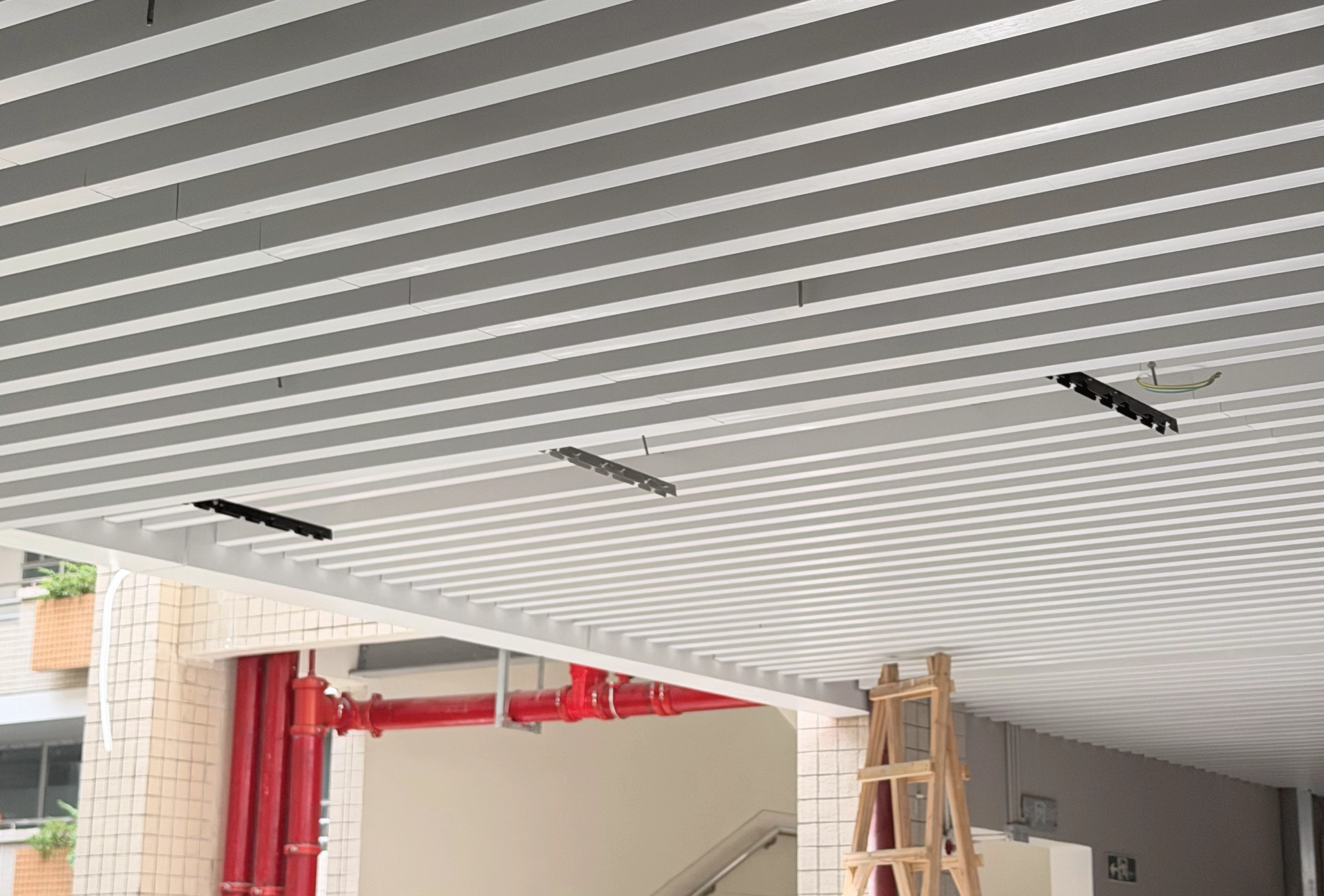 Guangzhou Baiyun University corridor: LINDELACR white U-baffle ceiling with fire pipe visible between slats