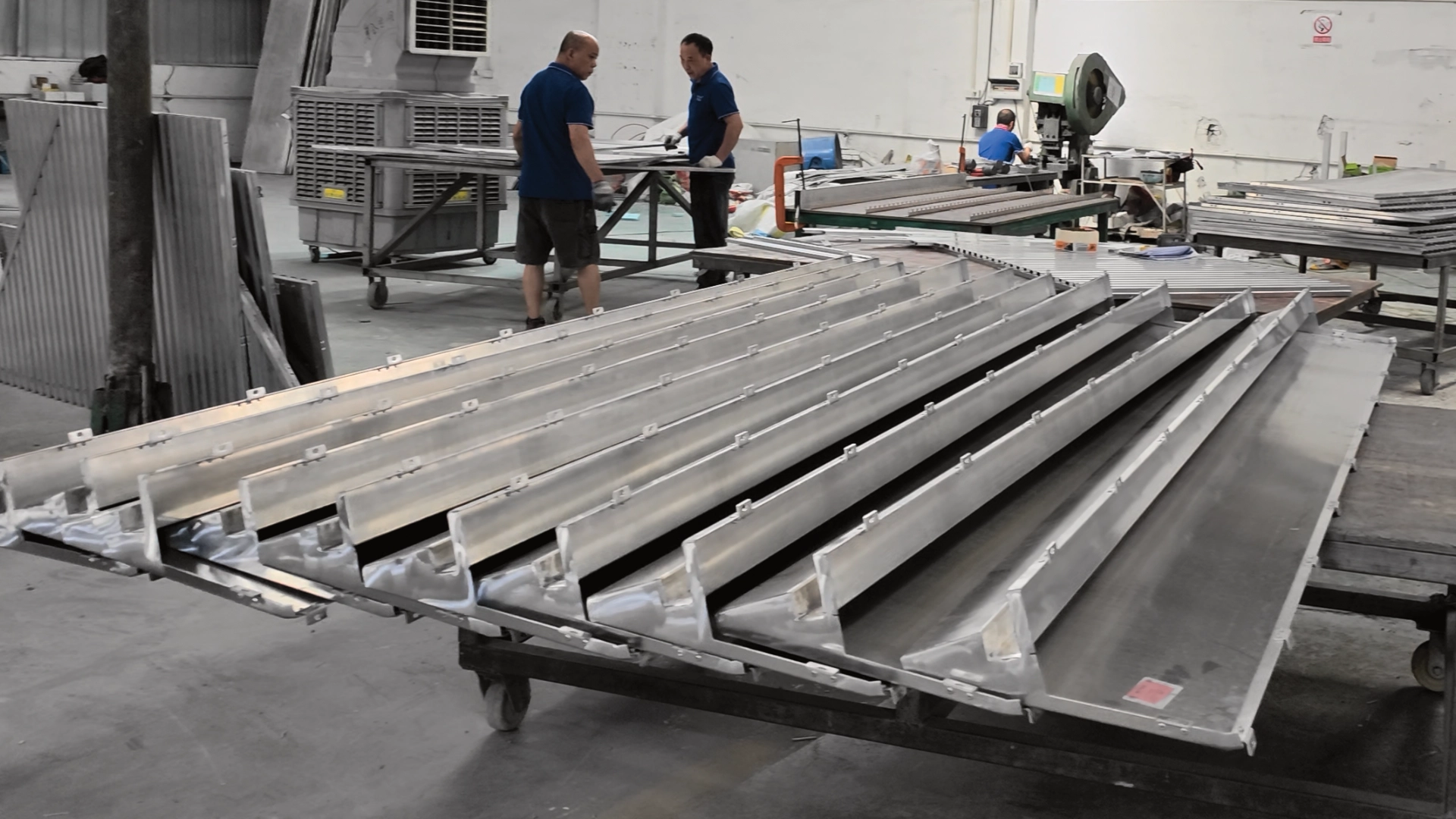 Mill-finish folded aluminum channels stacked on a cart in the Foshan shop before coating