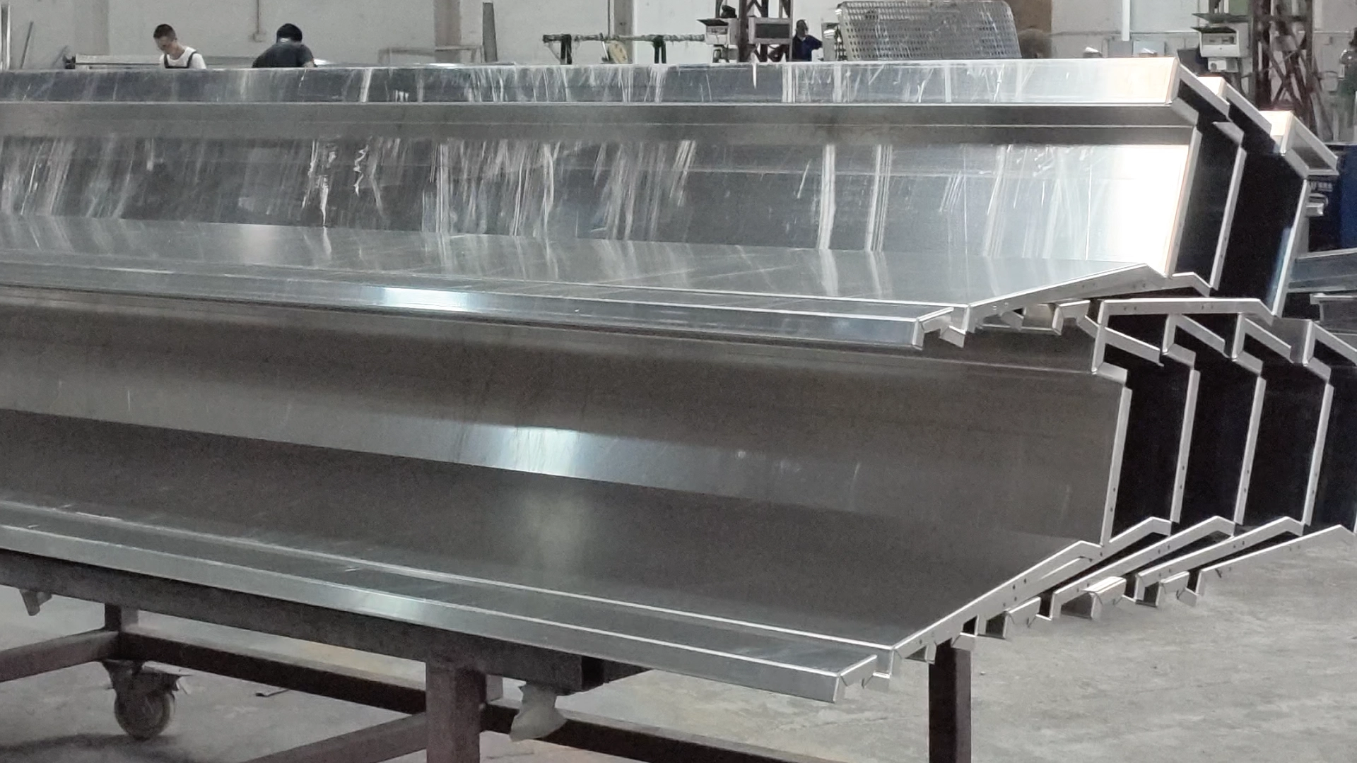 Stack of mill-finish aluminum panels with the return already folded and protective film still on