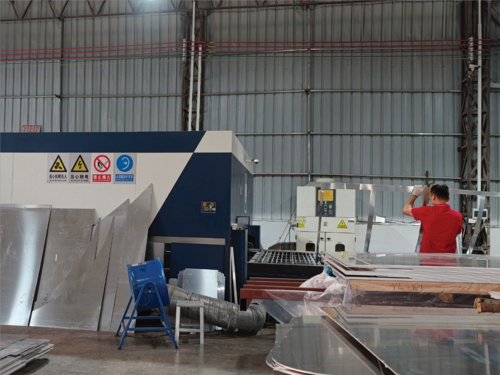 LINDELACR Foshan CNC cell: operator in red shirt handling mill-finish aluminum strip beside the enclosed cutter