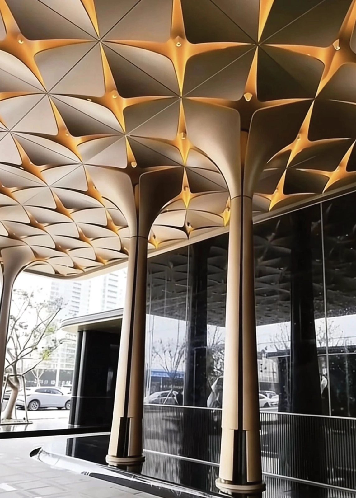 Gold 3D petal ceiling and flared aluminum column covers reflected in lobby glass, Thailand Golden Bay