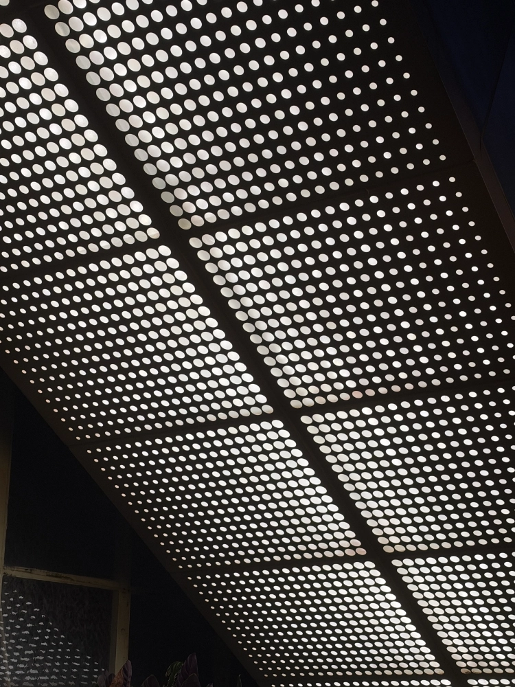 Perforated aluminum canopy at night with large round holes backlit, not a modular T-bar tile