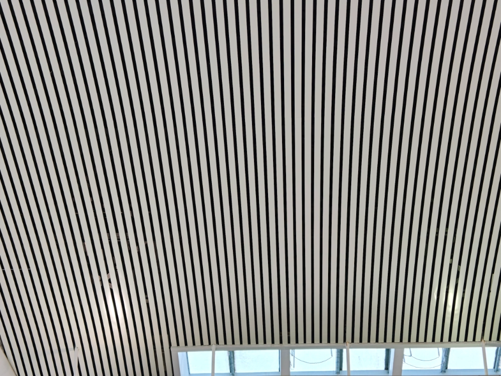 White linear aluminum baffles with open gaps between the blades and clerestory windows below