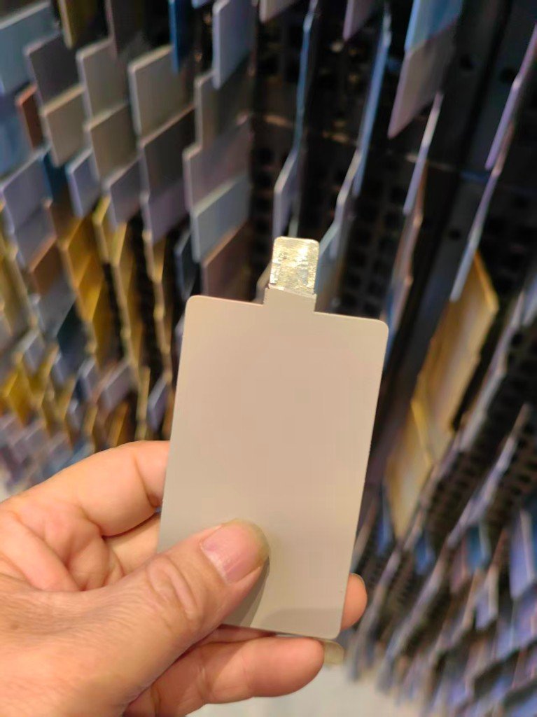 One coated aluminum color chip held in front of a finish rack. No color code is printed on the chip