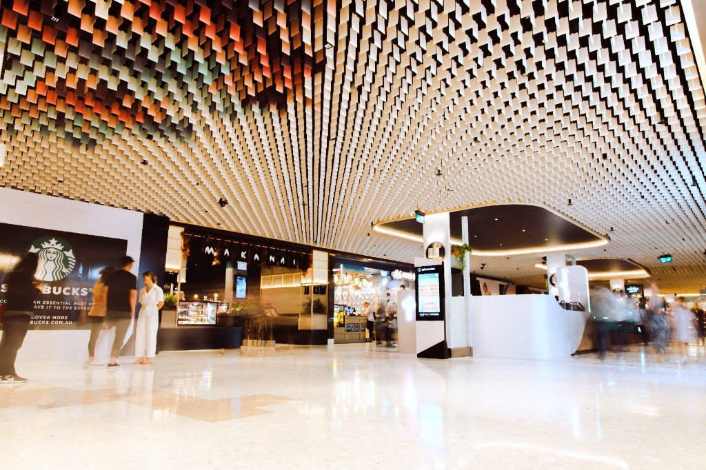 Radial aluminum blades over a mall concourse, shifting from a warm tone to white, with a curved black soffit