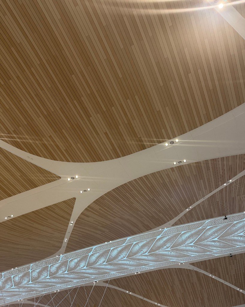 Wood-look linear ceiling with white branching ribs and a backlit perforated panel in a leaf pattern